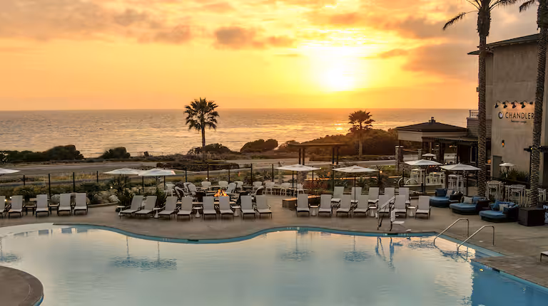 An image of a sunset over the Cape Rey Hotel pool and Pacific Ocean view.