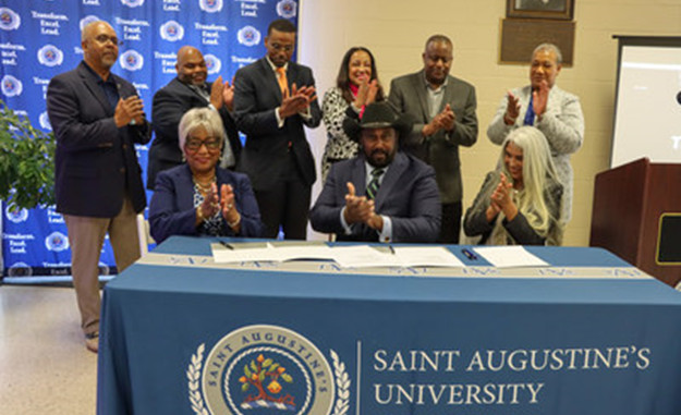 Nine people clapping at a signing ceremony