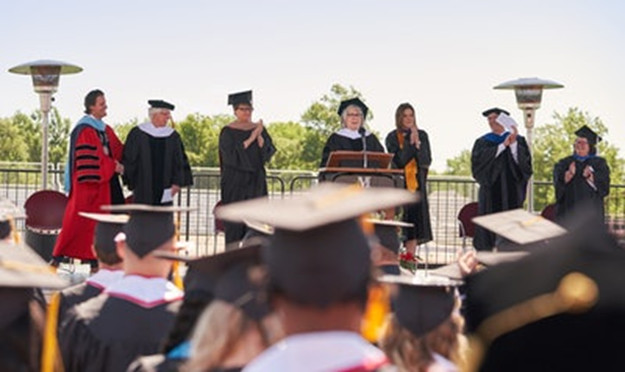 Speaker in academic robes at podium with audience clapping