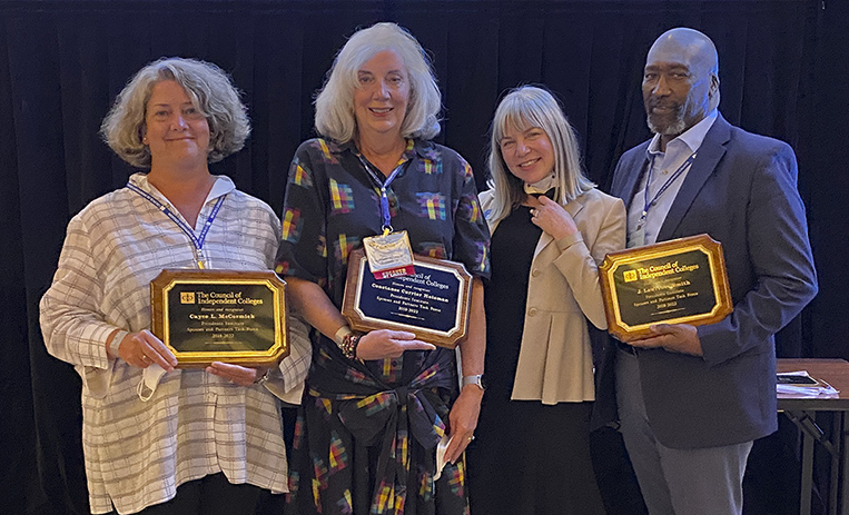 Three spouses holding awards pose with Marjorie Hass