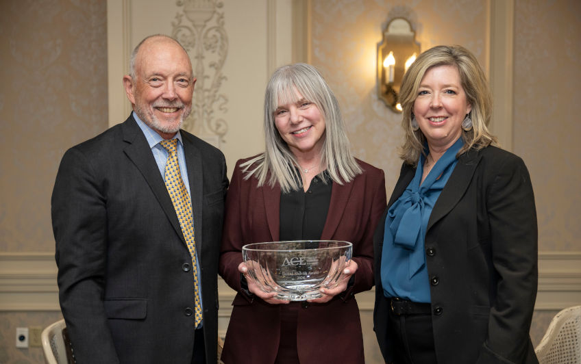 Marjorie Hass holding glass bowl award standing between Ted Mitchell and Debra Frey