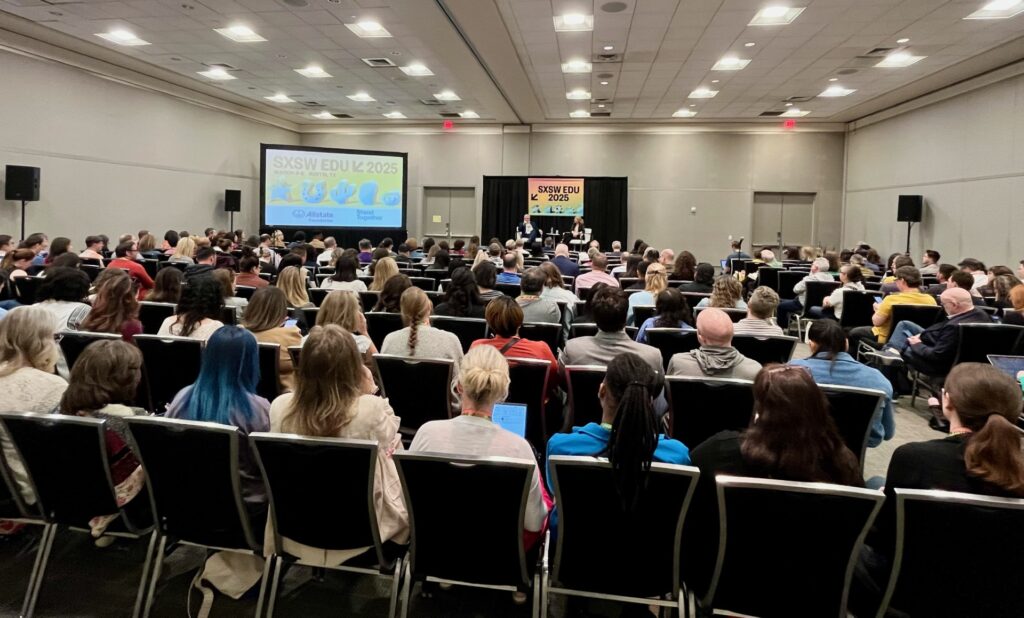 Participants of the 2025 SXSW EDU gathering listening to two speakers in a large room