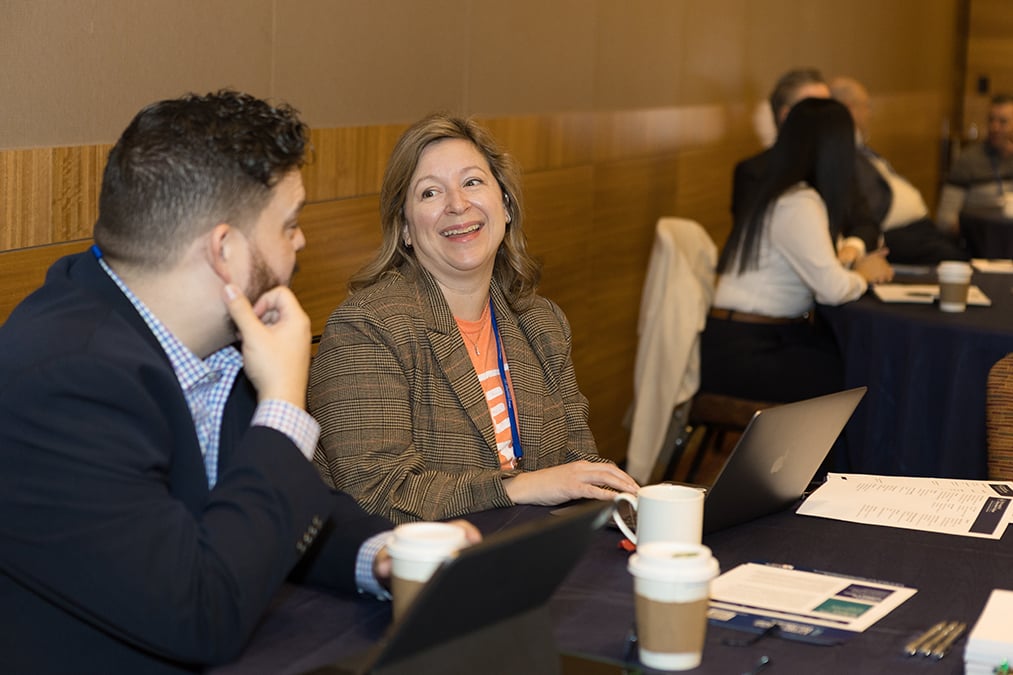 Two participants speak together while seated at a table