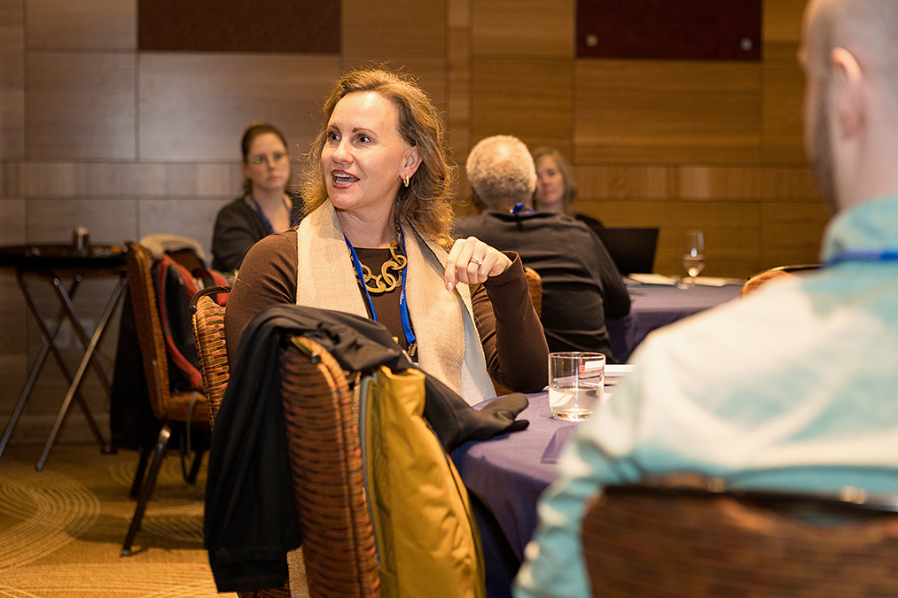 Participants seated at roundtables listen to a session speaker