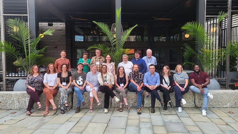 Group photo of participants seated outside along stone wall
