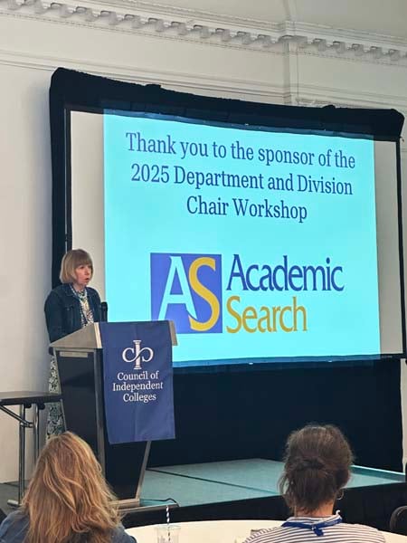 Speaker presents from podium with Academic Search sponsor acknowledgement on screen