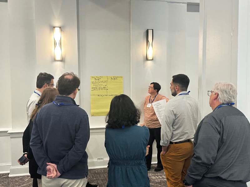 Participants discuss and write ideas on poster hanging on wall
