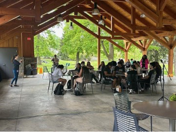 Student presents to seated participants in covered outdoor venue