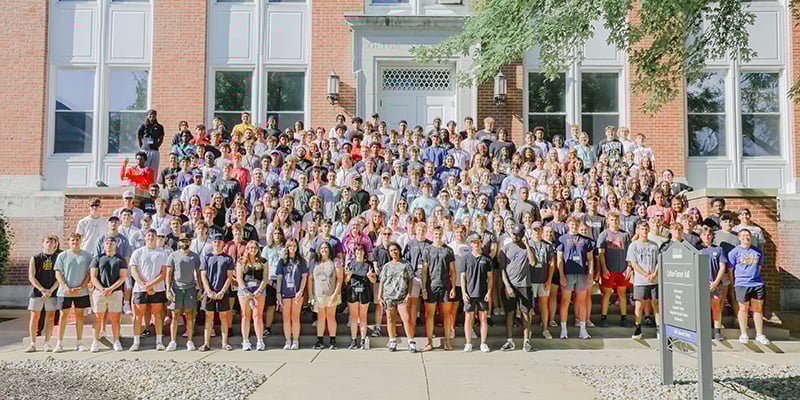 Large number of students standing outside campus building on steps for group photo