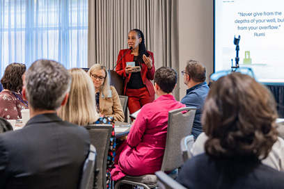Presenter speaks while standing at head of room beside projection screen