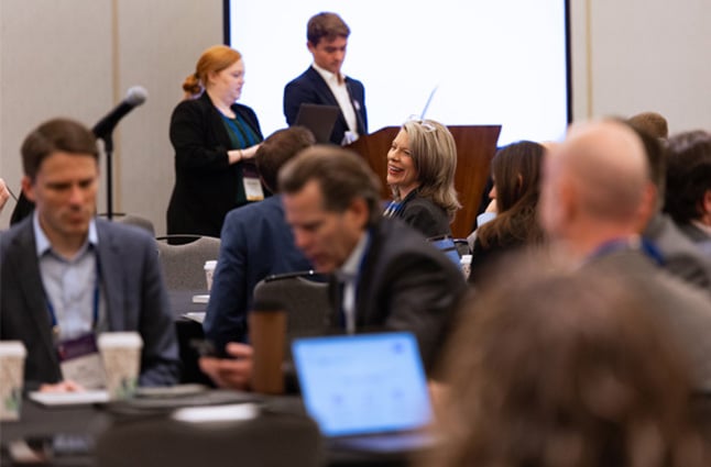Participants seated at roundtables during a concurrent session with speakers presenting from podium