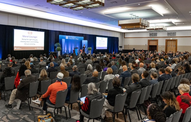 Participants seated in rows of chair during plenary session while speaker presents from stage