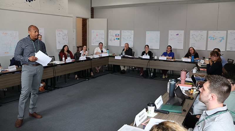Speaker presents while standing in middle of hollow square with seated participants