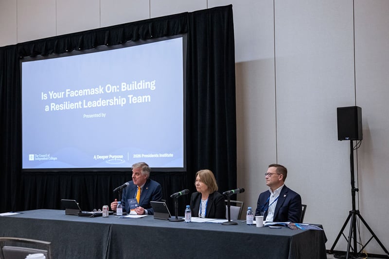 Three speakers sit at head table in front of projector screen