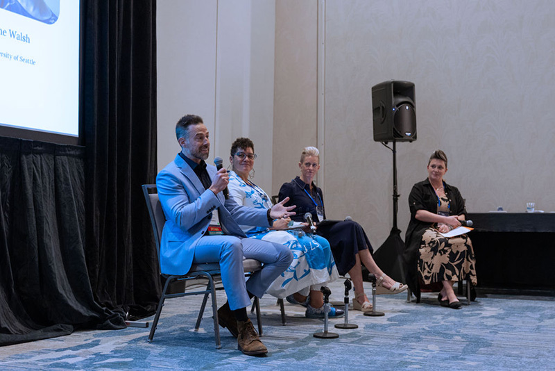 Four speakers sit in chairs in front of session room