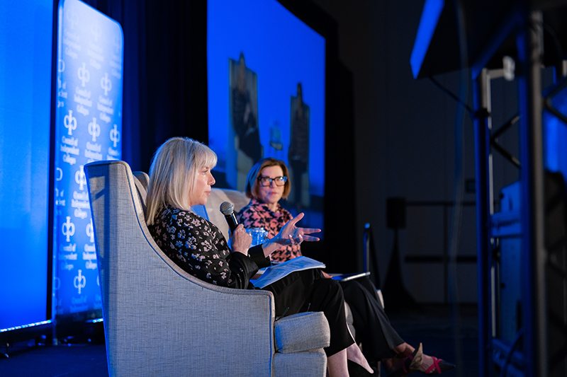 Barbara Mistick and Marjorie Hass sit on chairs on stage