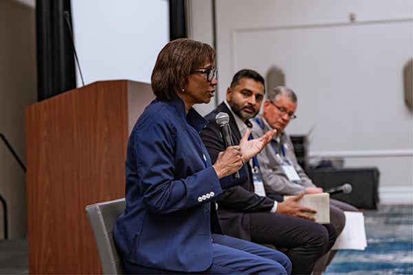 Panel of speakers seated in chairs speaking into microphones