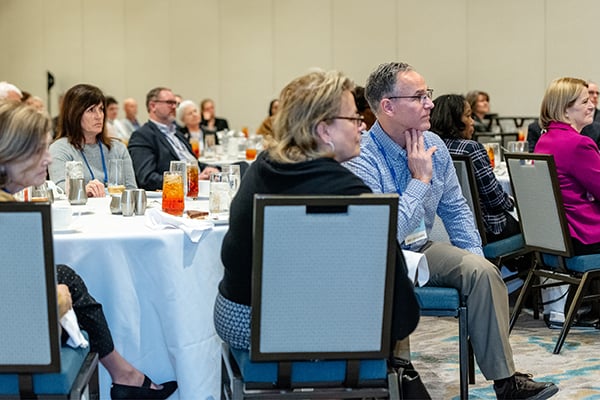 Participants seated at roundtables listen to presentation