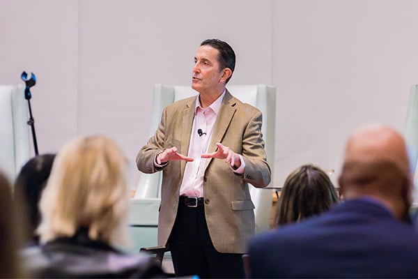 Speaker stands in front of seated participants speaking and gesturing with his hands