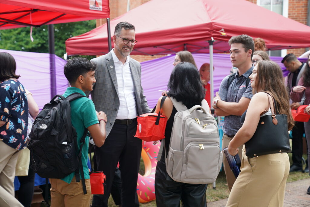 A group of people talk in a circle at an event on a college campus.