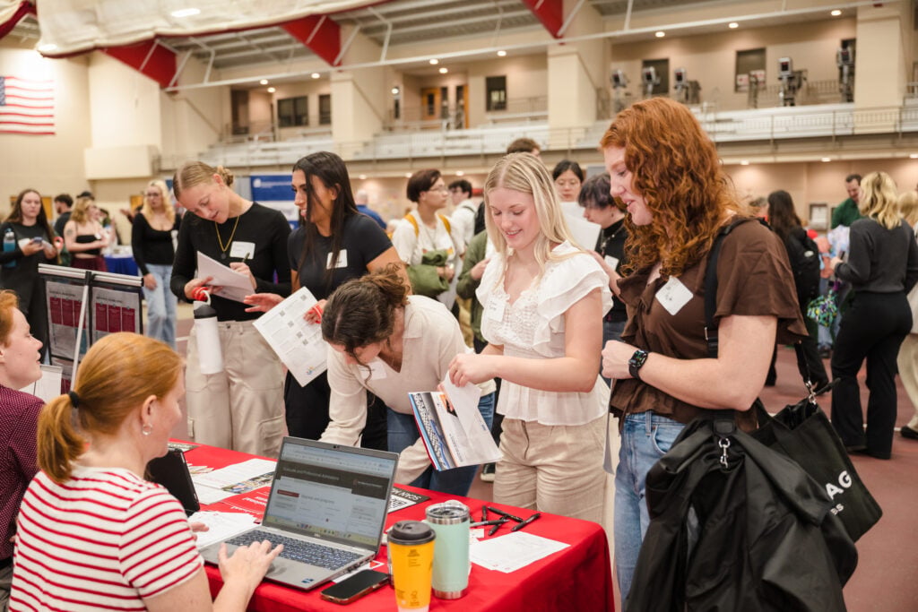 Students stand around a table at a campus event.